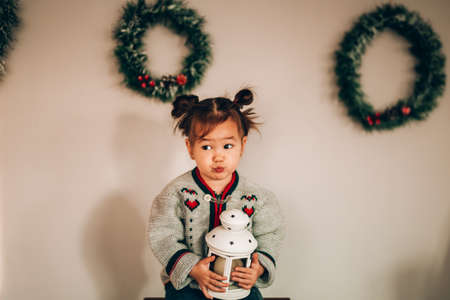 Little girl holding a white lantern in her hands. Christmas wreaths hang in the background....
