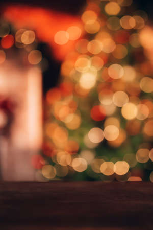 Beautiful blurred Christmas background. In the foreground is a wooden table. In the background there is a Christmas tree and a fireplaceの写真素材