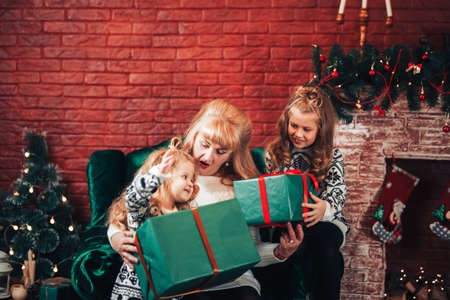 Grandmother gives children Christmas gifts in green packaging. Christmas mood. In the background there is a fireplace and a green armchair.の写真素材