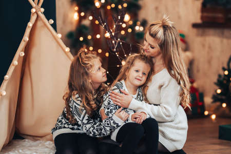 Children with mom sitting hugging on against a tent and a Christmas tree. Christmas mood. Celebrate the holiday with the whole family.の写真素材