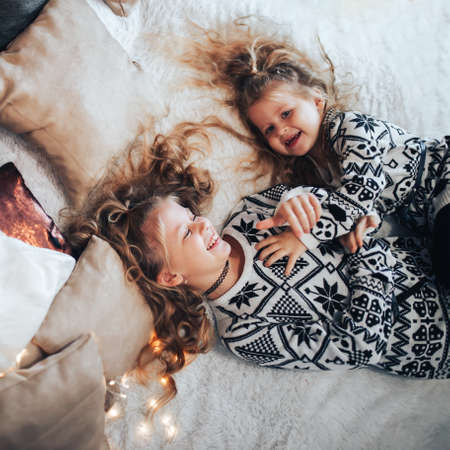 Children playing on a large bed. Friendly family concept. In the background there are lights from a garland.の写真素材