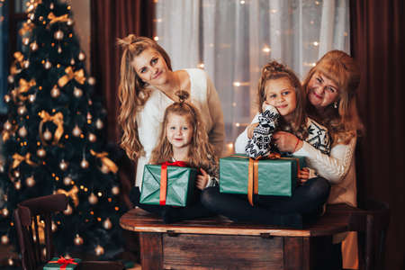 Children with mother and grandmother in their hands holding boxes with gifts in green packaging. Christmas mood. Celebrate the holiday with the whole family. Generation of women.の写真素材