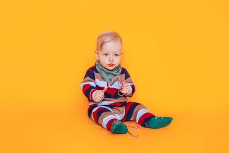 A child in Christmas pajamas sits against a yellow background. Christmas mood.