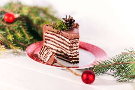 Chocolate cake on a red and white plate with a gold fork. Against the background of a branch of a Christmas tree and a decoration for the Christmas tree. Christmas mood.の写真素材