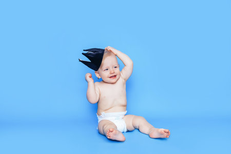 Little boy sits in front of a blue background. On the head is a black crown.の写真素材