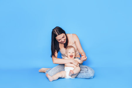 A young mother plays with her little son against a blue background. Adoption and childcare.の写真素材