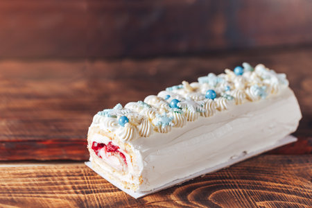 Beautiful white cake roll in front of a wooden background. The cake has snowflake-shaped confectionery decorations.の写真素材