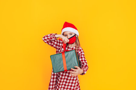 Child holding large boxes with gifts. There is a Santa hat on her head, and a medical mask on her face. Christmas mood. A perfect photo for a Christmas advertisement during a pandemic.の写真素材