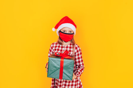 Child holding large boxes with gifts. There is a Santa hat on her head, and a medical mask on her face. Christmas mood. A perfect photo for a Christmas advertisement during a pandemic.の写真素材