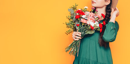 Woman holding a large bouquet of flowers in a green dress on a yellow background.の写真素材