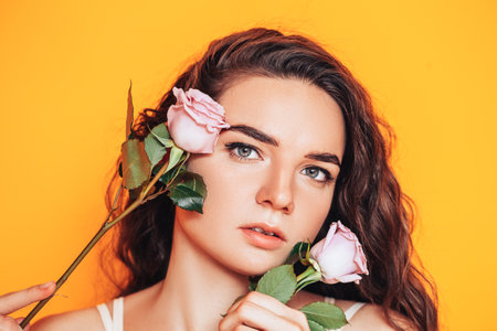 Young woman on a yellow background with pink roses near her face.の写真素材