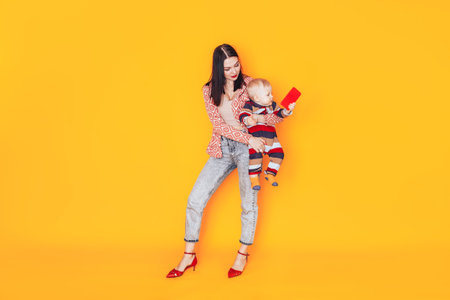 Mom with children in front of a yellow background. A happy family without a father. Mom holding a small child.の写真素材
