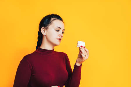 A woman in a red sweater holds a delicious zefir in her hands against a yellow background. Diet conceptの写真素材