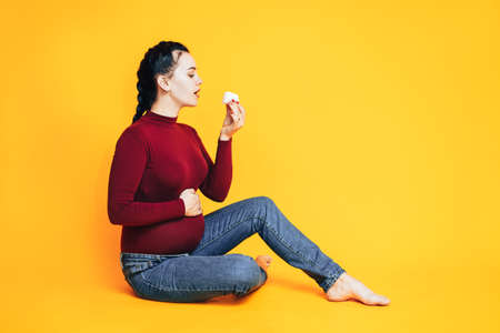A pregnant woman in a red sweater and blue jeans against a yellow background. Caring for the health of pregnant women.の写真素材