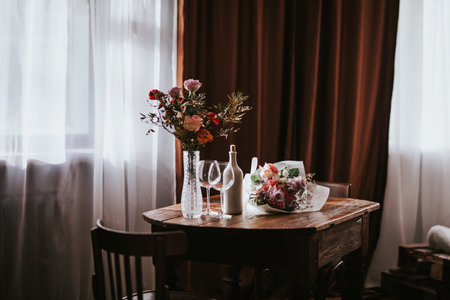 Glass vase with flowers on a wooden table in front of a light background. On the table are a bottle and glass wine glasses. Romantic mood for Valentine's day. Woman day, gift 8 march.の写真素材