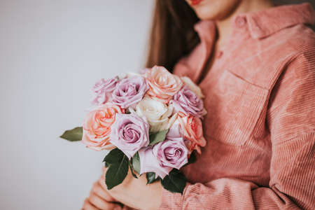 A woman in a pink sweater holding a bouquet of flowers in front of a white background. Woman day gift, 8 march.の写真素材