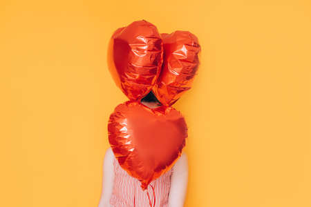 Girl holding heart-shaped balloons in her hands against a yellow background. Gift for valentine day, 14 february and womens day 8 march.の写真素材