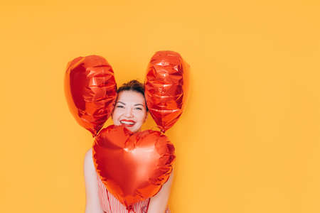 Girl holding heart-shaped balloons in her hands against a yellow background. Gift for valentine day, 14 february and womens day 8 march.の写真素材