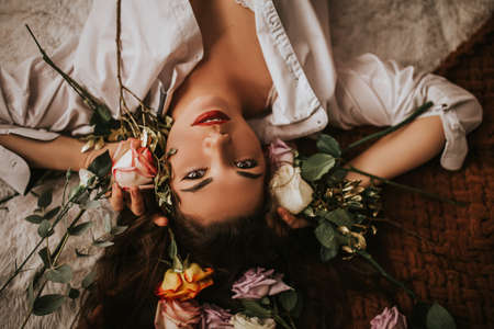 A woman in a white shirt lies on a bed with flowers. Valentine's day gift. Woman day gift, 8 marchの写真素材