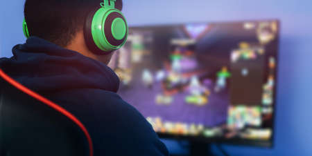 A young man playing a computer game on professional armchair against monitor in green headphones, live stream, esports. blue backgroundの写真素材
