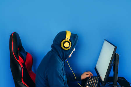 The gamer sits on a gaming chair and plays computer games. The player has yellow headphones on his head.の写真素材