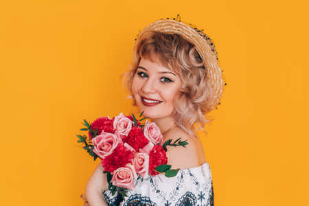 A woman in a dress holding a beautiful bouquet of flowers in front of a yellow background. Holiday gift.の写真素材