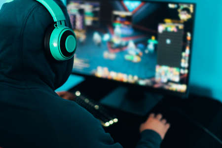 The gamer sits on a gaming chair and plays computer games. The player has turquoise headphones on his headの写真素材