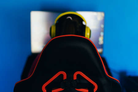 The gamer sits on a gaming chair and plays computer games. The player has yellow headphones on his headの写真素材