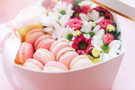 Macarons with flowers of different kinds in a box in the shape of a heart against a pink background. A gift for any occasion.の写真素材