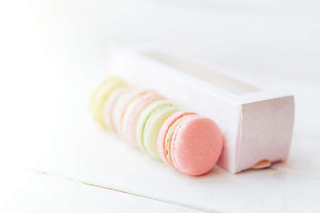 Macarons of pink color lie in a row, next to it lies a packing box against a wooden background. An...