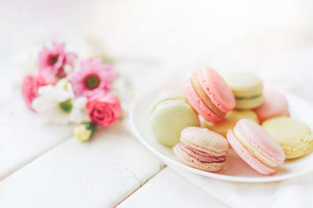 A full plate of macaroons lie in a plate of different colors, next to the plate is a small bouquet of flowers against a white background.の写真素材