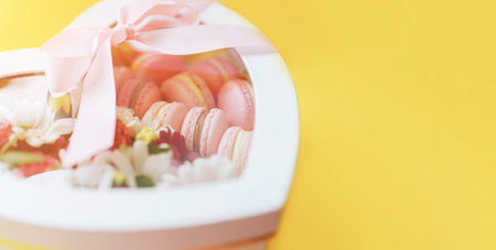 Macarons with different types of flowers in a box in the shape of a heart against a yellow background. A gift for any occasionの写真素材