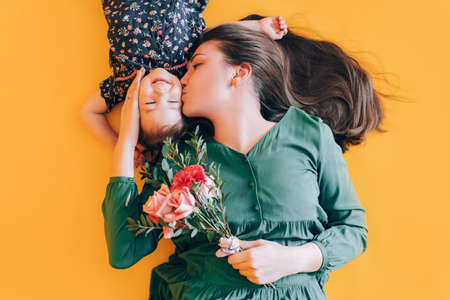 Mom and daughter are playing on a yellow background. Child gives mom flowers for a holiday.