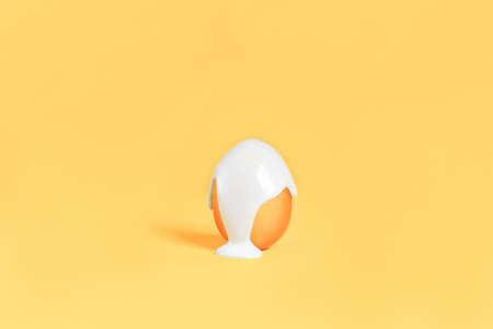 Bright white paint sticks down the golden egg against yellow background. Preparing for the religious holiday Easter, painting eggs for the event.の写真素材