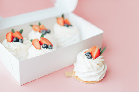 Delicious cakes covered with white and berry cream standing in box against pink backgroundの写真素材