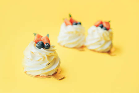 Delicious pastries covered with white and berries cream standing in row against yellow background