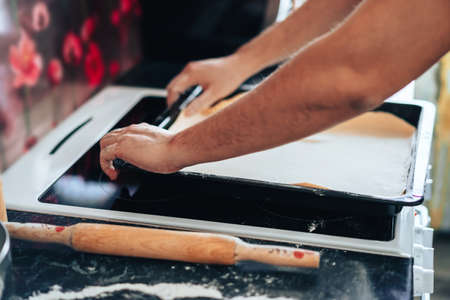 Man makes pizza at home in the kitchen. Places the dough on baking sheet
