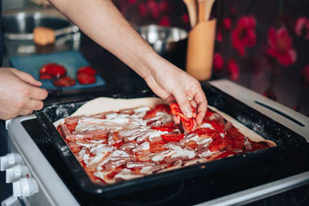 Man makes pizza at home in the kitchen. Lays out ingredients on the rolled doughの写真素材