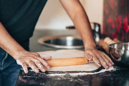 Man makes pizza at home in the kitchen. Rolls out the dough with rolling pinの写真素材