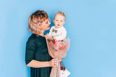Woman in dress holding little boy in her arms and holding beautiful bouquet of flowers in against...