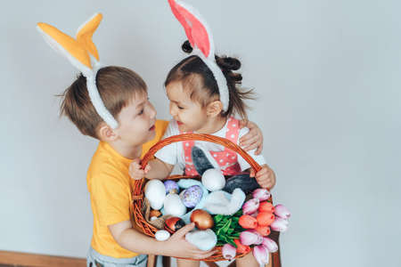 Little girl and boy dressed as rabbit holding large basket filled with eggs and tulips against white background.の写真素材