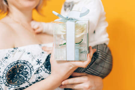 Woman in dress holding little boy in her arms and holding beautiful flower in against yellow background. Holiday gift.の写真素材
