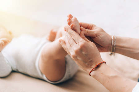 Caring mother gives foot and leg massage to her newborn baby. Caring for the health of children.の写真素材