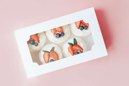 Delicious cakes covered with white and berry cream standing in box against pink background.の写真素材