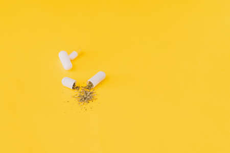 White capsule with dry herbsal inside, on yellow background.の写真素材