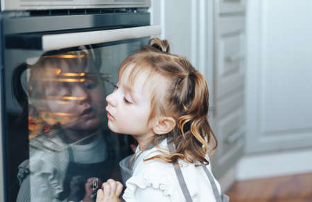 Child leaned against oven. Little girl is waiting for the cookies to be cookedの写真素材