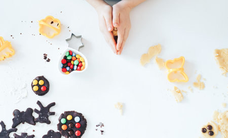 Hands of Child cutting chocolate and vanille cookie cutters at white table. Flat lay.の写真素材