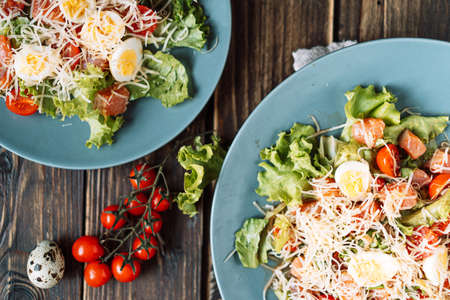 On wooden table, two plates with salad, quail eggs and cherry tomatoes.の写真素材