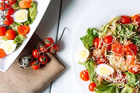 Two plates with quail egg and cherry tomato salad on white boardsの写真素材