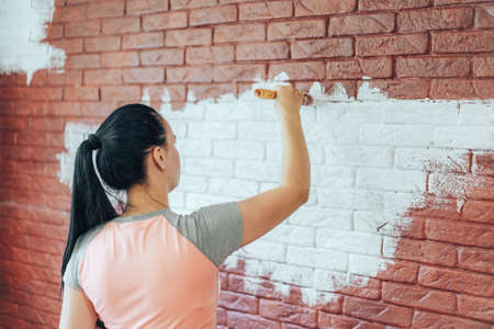 Girl with brush paints brick wall with white paint.の写真素材